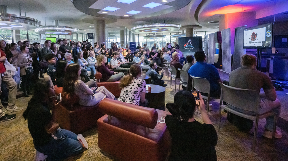 A group of people sitting in front of two television screens.